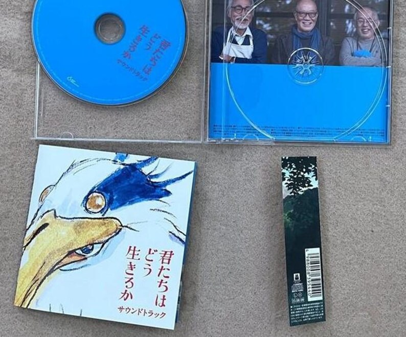 May include: A blue CD case with a white and blue bird illustration on the front. The text on the front reads "曾たちは どう 生きるか サウンドトラック".