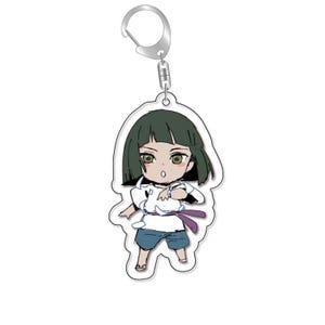 以下が含まれることがあります： 緑色の髪をした漫画のキャラクターが描かれたキーホルダー。白いシャツと青いショートパンツを着て、紫のリボンを持っています。キャラクターは驚いた表情をしています。
