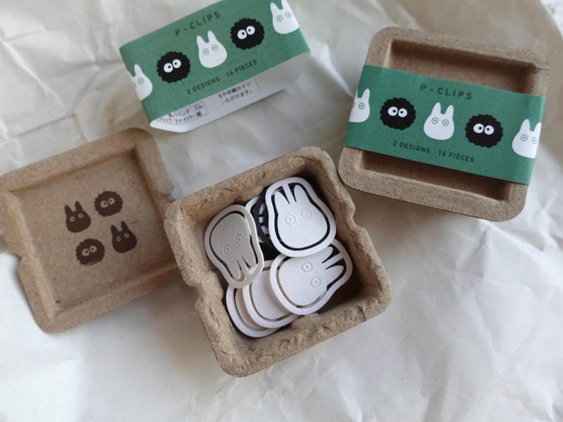 May include: A set of 14 paper clips in two designs, featuring a white and black cartoon character. The clips are packaged in a small, brown cardboard box with a green label that reads "P-Clips 2 Designs 14 Pieces".