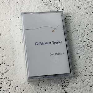Pu&ograve; includere: Una cassetta bianca con un design nero e oro. Il testo "Ghibli Best Stories" e "Joe Hisaishi" &egrave; stampato sul lato anteriore della cassetta.