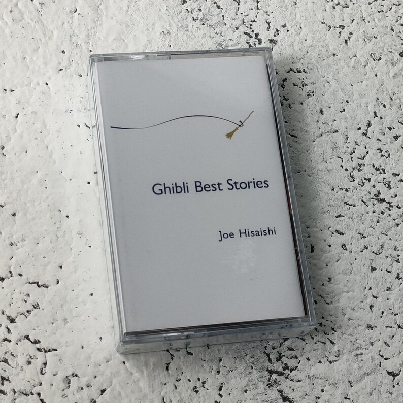 Pu&ograve; includere: Una cassetta bianca con un design nero e oro. Il testo "Ghibli Best Stories" e "Joe Hisaishi" &egrave; stampato sul lato anteriore della cassetta.