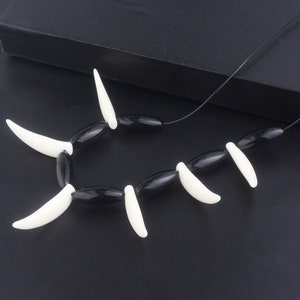 May include: A black and white necklace with oval black beads and white fang-shaped pendants.