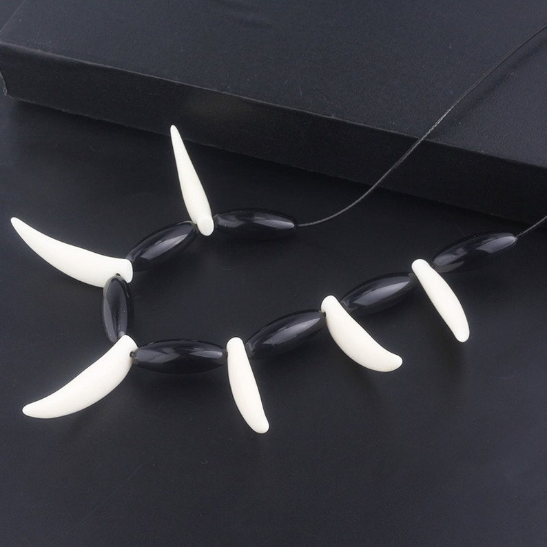 May include: A black and white necklace with oval black beads and white fang-shaped pendants.
