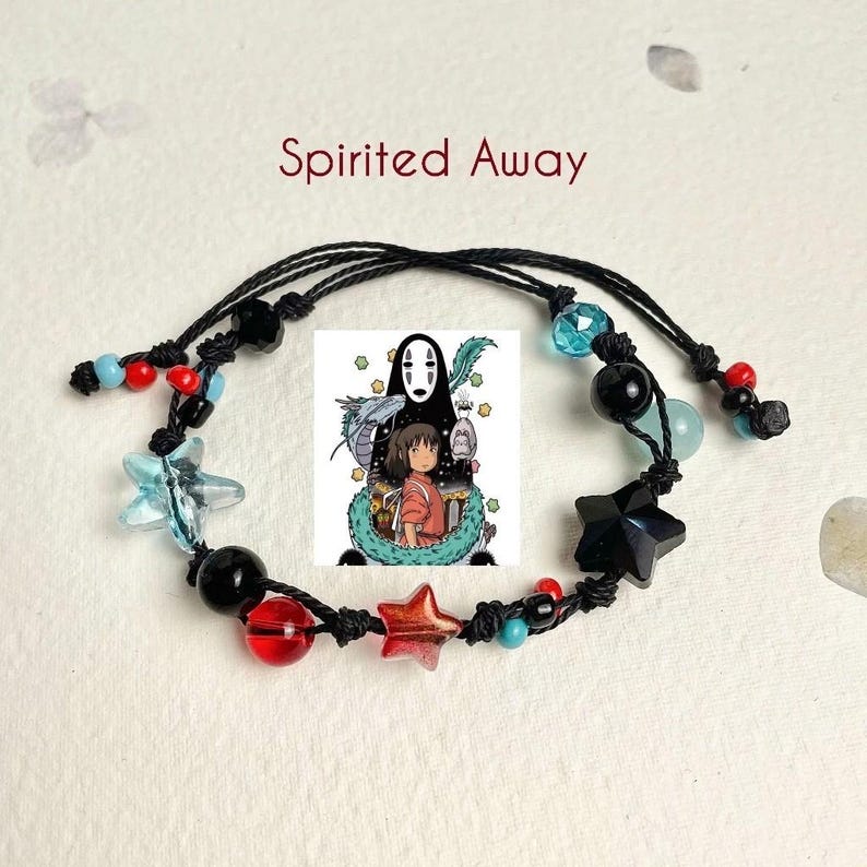 Puede incluir: Un brazalete de cuerda negra con cuentas rojas, azules y negras, y abalorios en forma de estrella. El brazalete presenta un abalorio con una imagen de personajes de la pel&iacute;cula animada "El viaje de Chihiro".