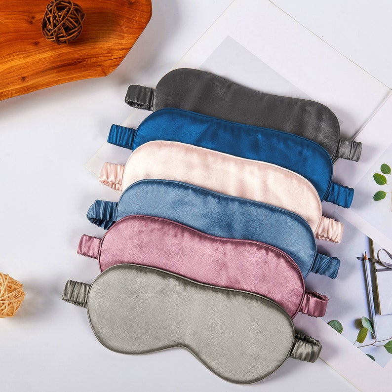 May include: Six silk sleep masks in a variety of colours, including grey, blue, pink, and beige. The masks are stacked on top of each other, with the grey mask at the bottom and the beige mask at the top.