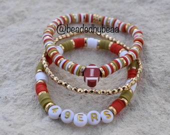 Peut inclure: Ensemble de trois bracelets en perles rouges, blanches et vertes avec un charme de football et un charme "49ERS".
