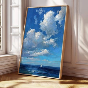 Puede incluir: Pintura enmarcada de un paisaje marino con un cielo azul brillante lleno de nubes blancas y esponjosas. El océano es de un azul profundo con un pequeño velero. La pintura está en un marco de madera clara.