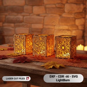 May include: Three wooden candle holders with intricate floral and swirl cut-out designs. The warm glow of the candles inside illuminates the detailed patterns. The candle holders are on a table with fall leaves.