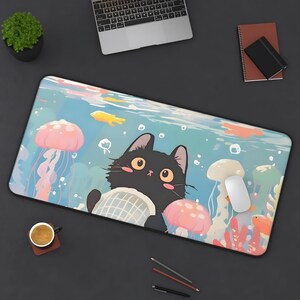 Op de afbeelding: Een zwarte kat met witte ogen zit op een blauwe en witte gepatroneerde muismat met een kwal en andere zeedierenontwerpen. De muismat ligt op een donkergrijs oppervlak.