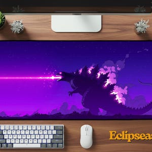 May include: A large rectangular mousepad featuring a purple and black illustration of Godzilla emitting a pink laser beam. The background is a gradient of purple and black with a starry sky. The word "Eclipseas" is in the bottom right corner.