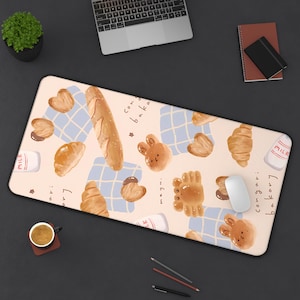 May include: A rectangular beige mousepad featuring a whimsical bakery theme. The design includes illustrations of bread, pastries, milk cartons, and a blue checkered pattern. The words "con bakari" are written on the mousepad.