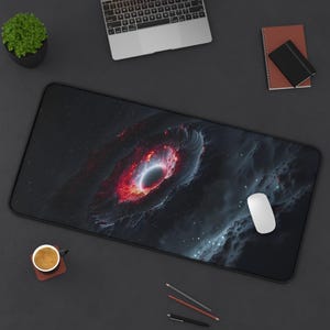 May include: A black and red galaxy-themed mousepad with a swirling nebula and a black hole in the center. The mousepad is on a dark gray surface.