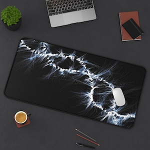 Puede incluir: Alfombrilla de ratón rectangular negra con un diseño abstracto blanco y azul. Un ratón de ordenador blanco descansa sobre la alfombrilla. La alfombrilla está sobre una superficie oscura con un portátil, una taza de café y artículos de papelería.