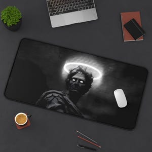 May include: Black and white desk mat featuring a statue with a glowing halo. The design includes a laptop, mouse, pencils, and a small potted plant. A cup of coffee sits on a coaster.