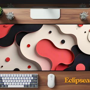 May include: A large rectangular mouse pad with a modern abstract design in red, black, and cream colors. The design features layered, organic shapes. A white keyboard and mouse are positioned below the pad. The word "Eclipseas" is printed in gold.