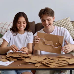 May include: A set of brown cardboard puzzle pieces and a flat sheet with die-cut shapes on a wooden table. The cardboard is light brown with a matte finish, featuring various animal-shaped cutouts and small connecting components for assembly.