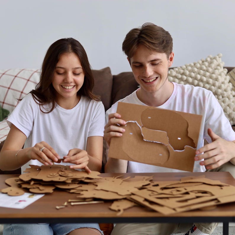 May include: A set of brown cardboard puzzle pieces and a flat sheet with die-cut shapes on a wooden table. The cardboard is light brown with a matte finish, featuring various animal-shaped cutouts and small connecting components for assembly.