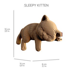May include: A layered cardboard sculpture of a kitten labelled SLEEPY KITTEN. The figure measures 10 cm in height, 15 cm in length, and 8 cm in width, featuring a tan, ribbed texture created by stacked corrugated cardboard layers.