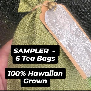 May include: A green burlap bag sampler containing six tea bags, with a tag that reads "MAMAKI TEA SAM Hawai'i Island Grown." The bag also has text that says "SAMPLER - 6 Tea Bags" and "100% Hawaiian Grown."