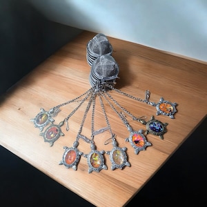 Può includere: Un set di otto infusori per tè in argento a forma di tartaruga. Ogni tartaruga ha un inserto in vetro di colore diverso con un motivo floreale. Gli infusori sono attaccati a catene d'argento.