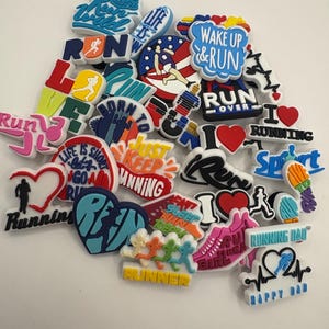 May include: A selection of vibrant shoe charms with running motifs. The charms display phrases such as "Run," "Wake Up & Run," and "Running Girl," alongside running shoe and runner silhouettes. The color palette includes red, blue, and yellow.