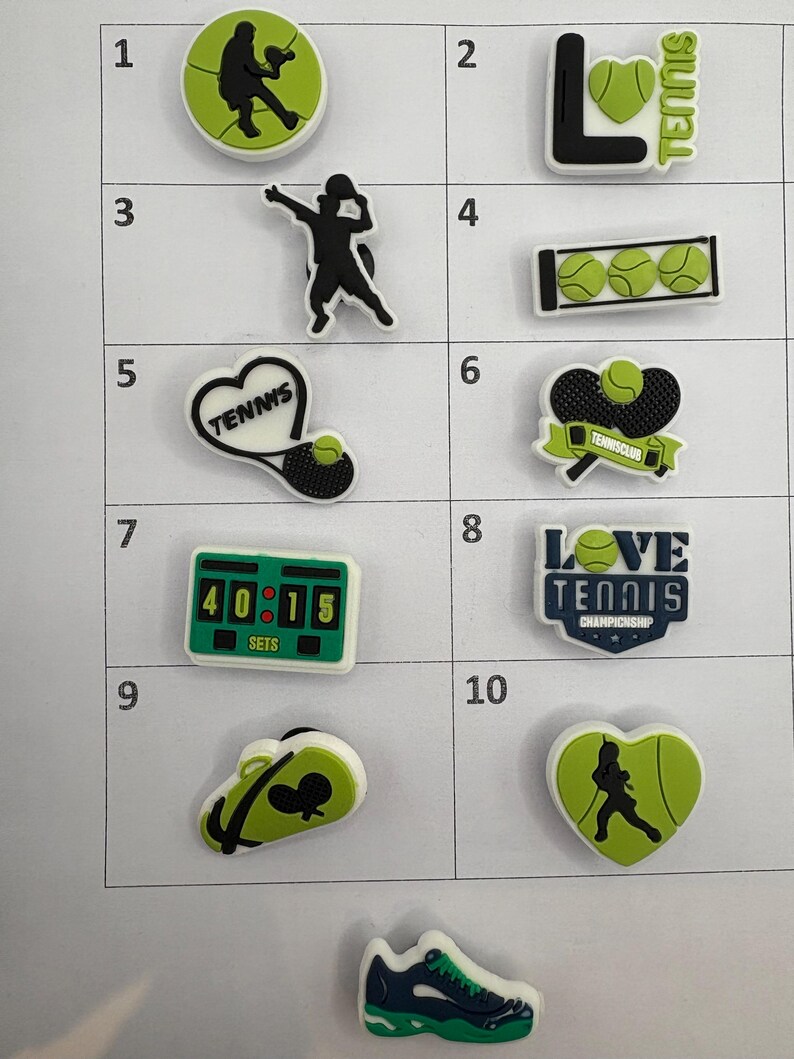 May include: Ten tennis shoe charms featuring various tennis-themed designs, including a tennis player, a tennis racket, a tennis ball, a heart with the word "Tennis" on it, a scoreboard, a tennis bag, and a heart with a tennis player inside. The charms are all white with green and black accents.