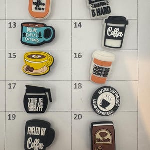 May include: A collection of coffee-themed charms in various shapes and colors. Designs include coffee cups, coffee beans, and phrases like "Fueled by Coffee" and "Coffee Because Adulting is Hard."