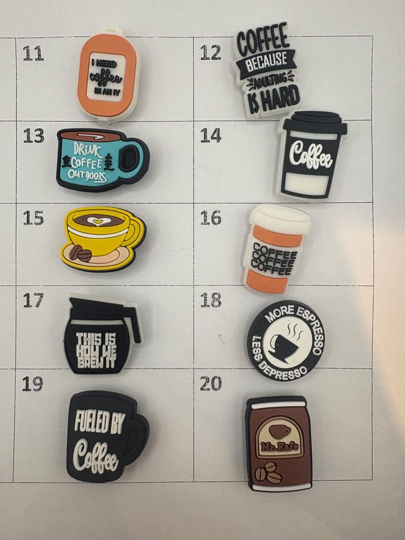 May include: A collection of coffee-themed charms in various shapes and colors. Designs include coffee cups, coffee beans, and phrases like "Fueled by Coffee" and "Coffee Because Adulting is Hard."