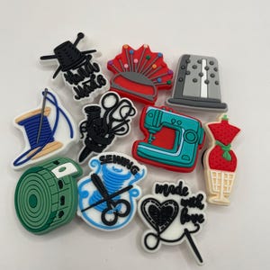 May include: A collection of 12 colourful sewing-themed charms, including a sewing machine, a spool of thread, scissors, a thimble, and a pincushion. The charms are made of silicone and have a variety of designs.