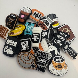 May include: A collection of coffee-themed charms in various shapes and colors. The charms feature coffee cups, coffee pots, and phrases like "Coffee for Life," "Fueled by Coffee," and "I Need More Coffee." The charms are designed for decorative purposes.