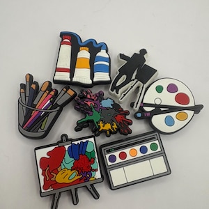 以下が含まれることがあります： 絵の具チューブ、ペン立て、画家、筆付きパレット、絵の具の飛び散り、絵画が飾られたイーゼル、カラフルな円が描かれた水彩絵の具セットなど、アートをテーマにした7種類のカラフルなシューズチャームのコレクション。