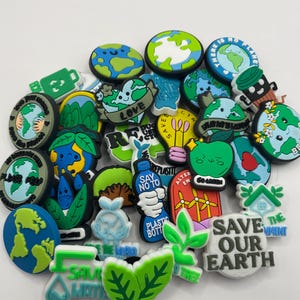 May include: A selection of vibrant shoe charms with eco-friendly designs. The charms feature the Earth, leaves, recycling symbols, and slogans such as "Save Our Earth" and "Say No To Plastic Bottles."
