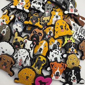 May include: A collection of colourful dog charm shoe charms featuring various dog breeds. The charms are made of rubber and have a 3D design. The charms are arranged in a pile and include a pink heart charm with a black dog silhouette.