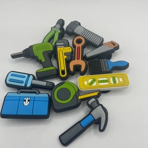 以下が含まれることがあります： ドリル、レンチ、のこぎり、ハンマー、メジャー、レベル、ペンチ、ブラシ、ツールボックスなど、カラフルなオモチャの工具のコレクション。これらの工具はプラスチック製で、本物の工具のように見えるように設計されています。