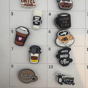 May include: A collection of coffee-themed charms with various designs and text. Includes a coffee pot, a coffee cup with "Coffee for Life", a coffee cup with "I need my space", and a charm that says "Caffeine Queen".