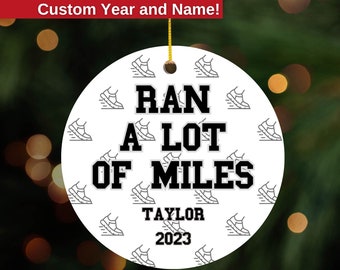 May include: White round Christmas ornament with a black and white running shoe pattern. The ornament says "Ran A Lot Of Miles" with the name "Taylor" and the year "2023" below.