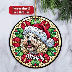 May include: A round Christmas ornament featuring a stained glass design of a dog wearing a Santa hat. The dog is a light brown and white breed with a red bow and the name "Murphy" written below it.