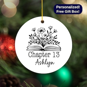 May include: White ceramic ornament with a black and white illustration of an open book with flowers growing out of it. The text "Chapter 13 Ashlyn" is printed below the book.