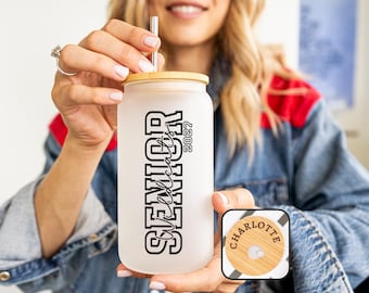 May include: A frosted glass tumbler with a bamboo lid and a stainless steel straw. The tumbler features the text "SENIOR Wildcats 2022" in black block letters. A small wooden lid with the name "Charlotte" is also visible.