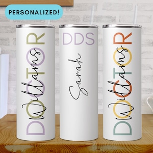 May include: Three white stainless steel tumblers with colorful geometric designs and personalized text. The tumblers are labeled "Doctor Williams", "DDS Sarah", and "Doctor Williams".