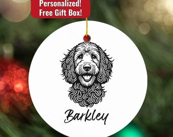 May include: White round ornament with a black and white illustration of a dog's face. The dog's name, "Barkley," is written in cursive below the image. The ornament has a gold string for hanging and a red bead at the top.