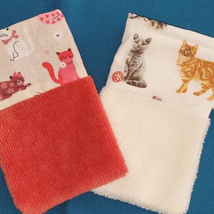 Peut inclure: Deux essuie-mains rectangulaires à suspendre avec des parties supérieures en tissu à motifs de chats et des parties inférieures texturées unies. L'un a une base corail, l'autre une base blanche. Chaque essuie-main possède une boucle.