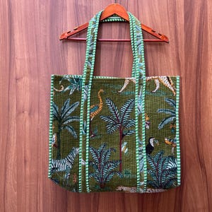 May include: A green tote bag with a white trim and a jungle print featuring zebras, toucans, and palm trees.