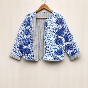 Peut inclure: Veste à imprimé floral bleu et blanc avec intérieur rayé. La veste est suspendue à un cintre en bois. La veste a un motif matelassé avec un motif floral bleu sur fond blanc. L'intérieur est rayé noir et blanc.