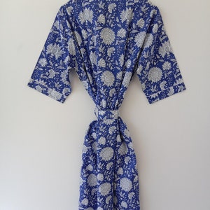 Op de afbeelding: Een blauwe katoenen badjas met een witte bloemenprint. De badjas heeft een strikceintuur en lange mouwen.