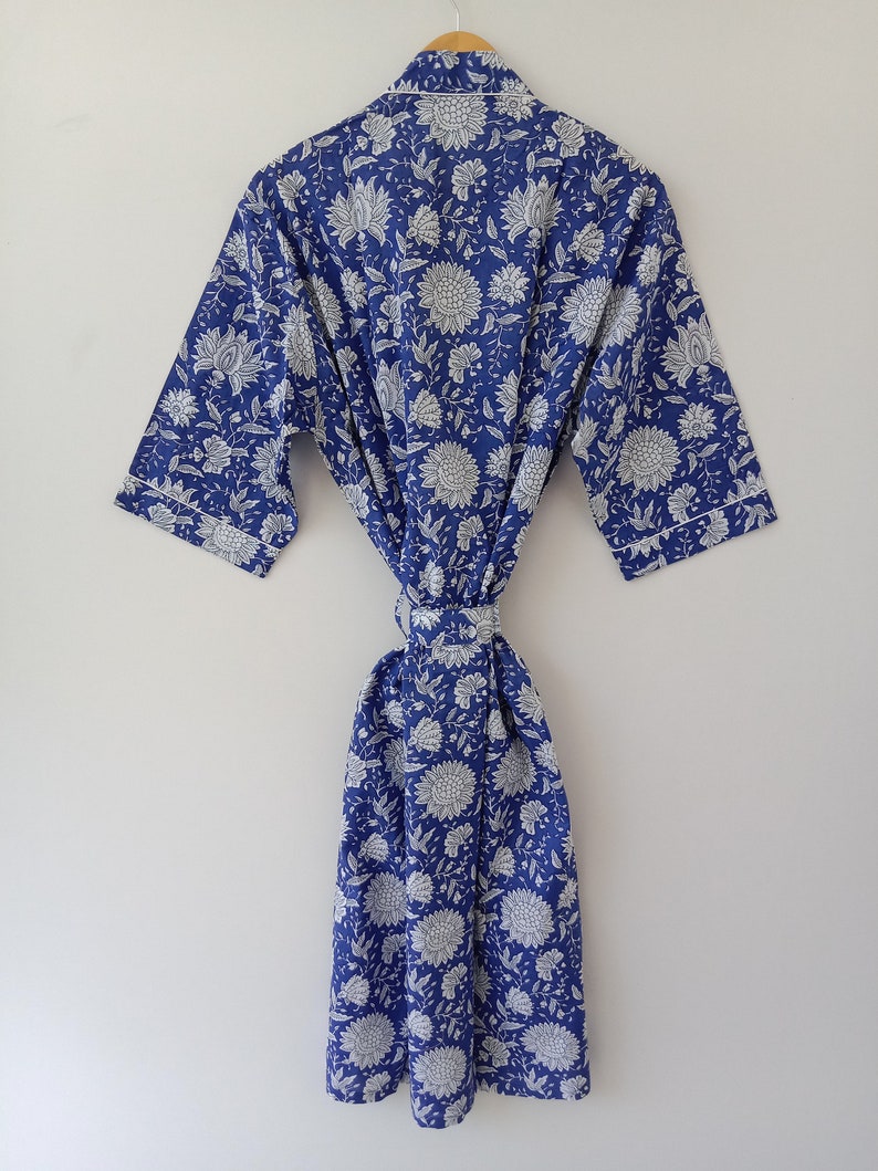 Op de afbeelding: Een blauwe katoenen badjas met een witte bloemenprint. De badjas heeft een strikceintuur en lange mouwen.