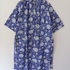 Op de afbeelding: Een blauwe katoenen badjas met een witte bloemenprint en witte bies. De badjas heeft een strikceintuur en twee zakken.
