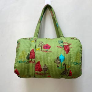 Può includere: Una borsa tote trapuntata verde con una stampa floreale colorata. La borsa ha due manici superiori e una chiusura a zip.