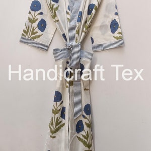 May include: White cotton robe with a blue floral pattern and striped trim. The robe features a tie closure and is hanging on a wooden hanger. The text "Handicraft Tex" is visible on the robe.