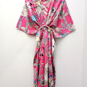 May include: A pink and white floral print kaftan with a tie at the waist. The kaftan has a V-neck and short sleeves.